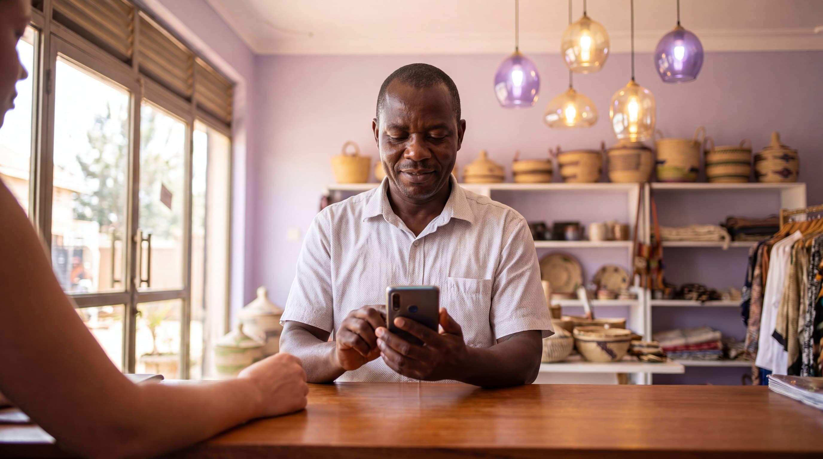 A shop owner in a Kampala storefront completing a mobile money payment on a phone at the counter